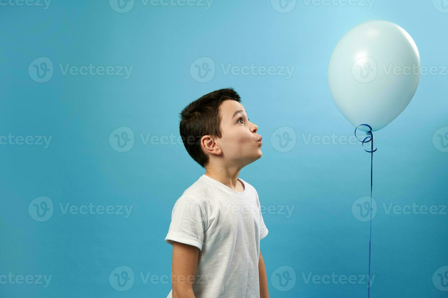 Cute schoolboy looking at a blue balloon on blue background photo