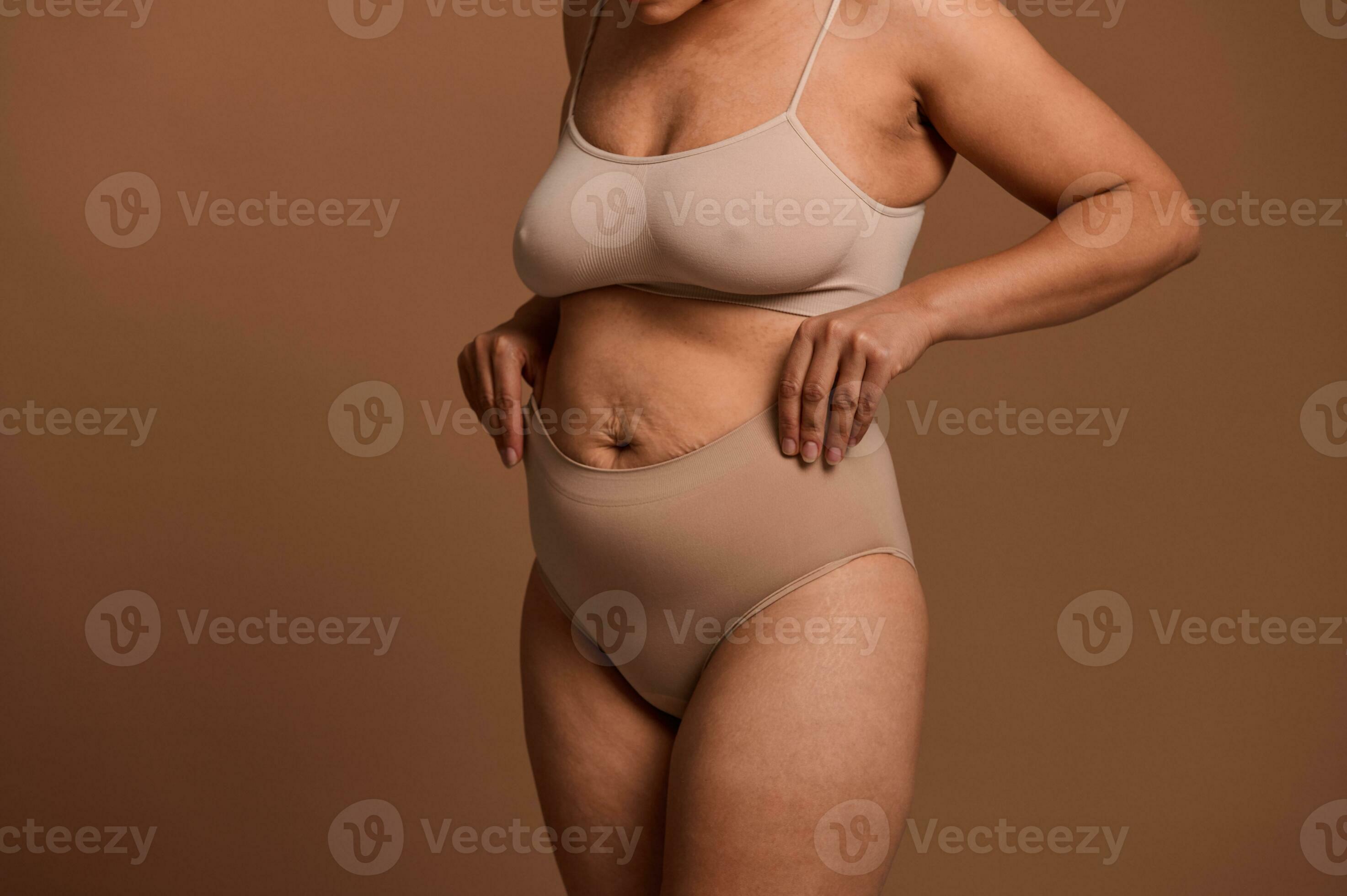 Cropped view of a woman in beige underwear laying her hands on her stomach  with relaxed muscles that have lost their tone and stretch marks after  pregnancy and childbirth. Body positive concept