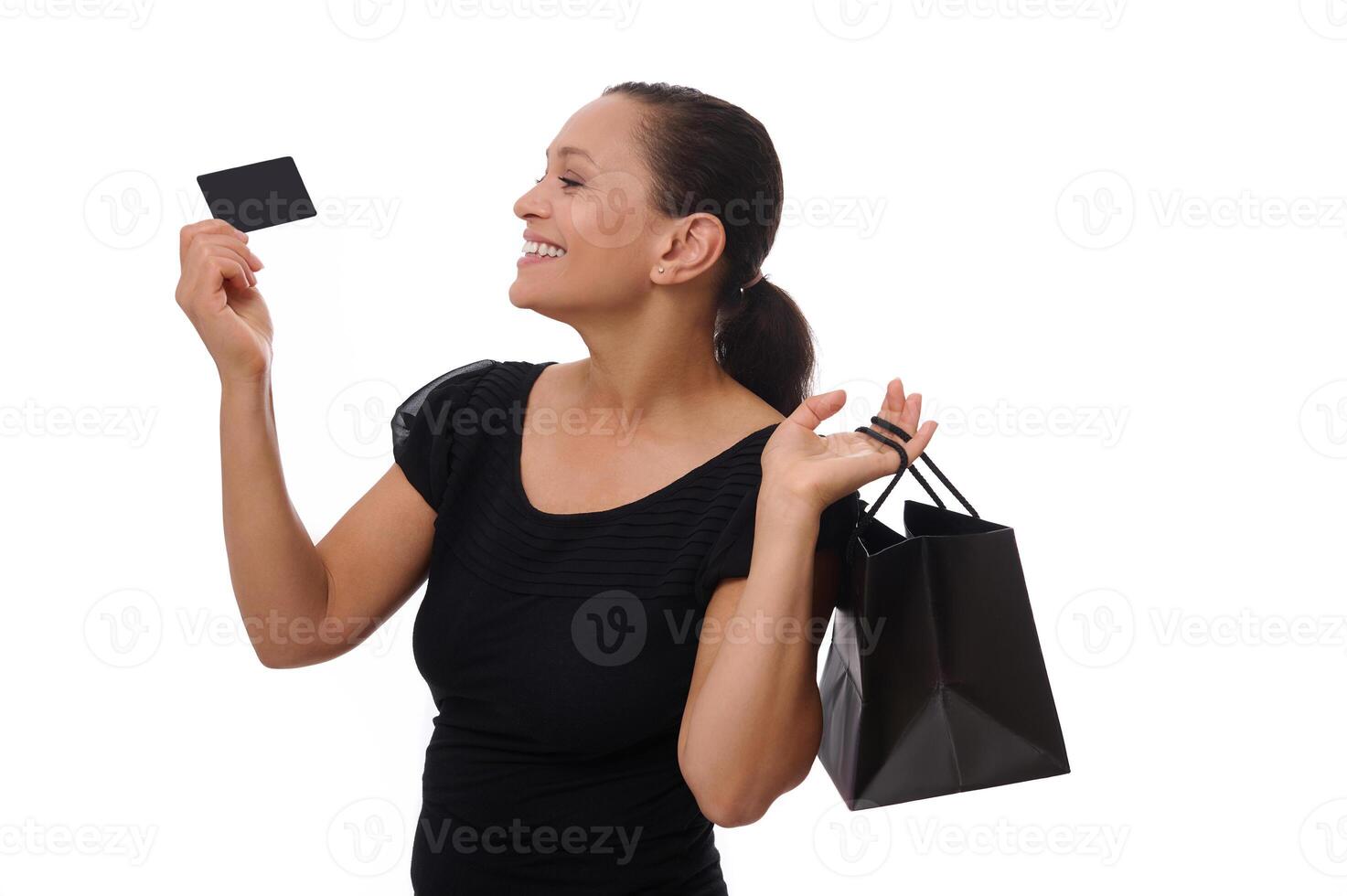 Portrait of young mixed race African American woman smiling with beautiful toothy smile holding shopping bags and credit or discount card in hands, standing against white background with copy space photo