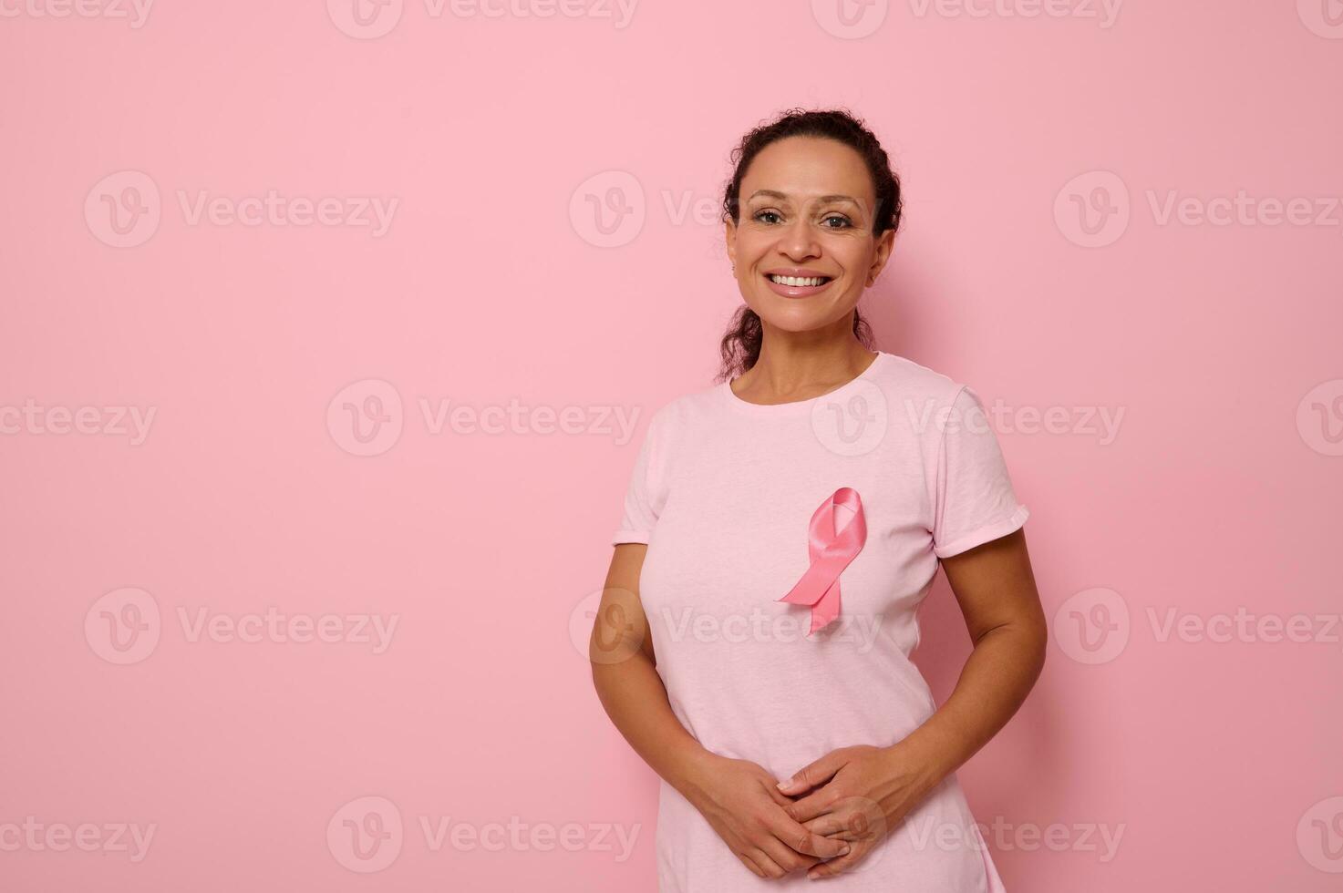 Smiling mixed race woman in pink T-shirt with pink satin ribbon symbolizing International Breast Cancer Day, expressing solidarity and support for breast cancer patients and survivors. 1 st october photo