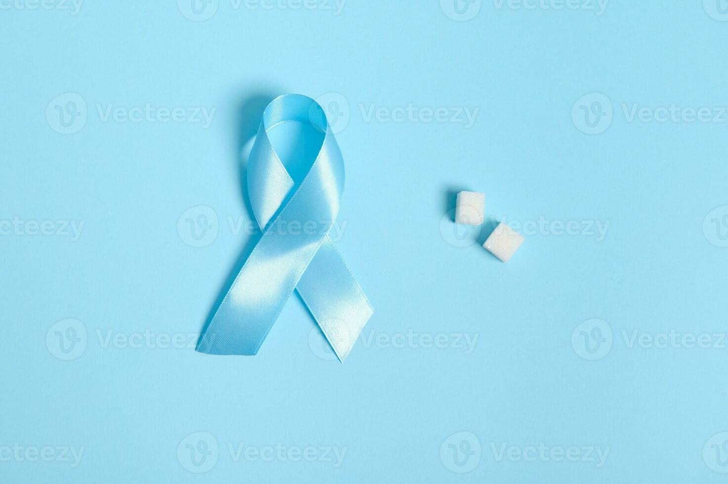 Flat lay of pure refined white sugar cubes and blue satin ribbon, symbol of World diabetes awareness day 14 November. Isolated over colored blue background, copy space for medical advertising. photo