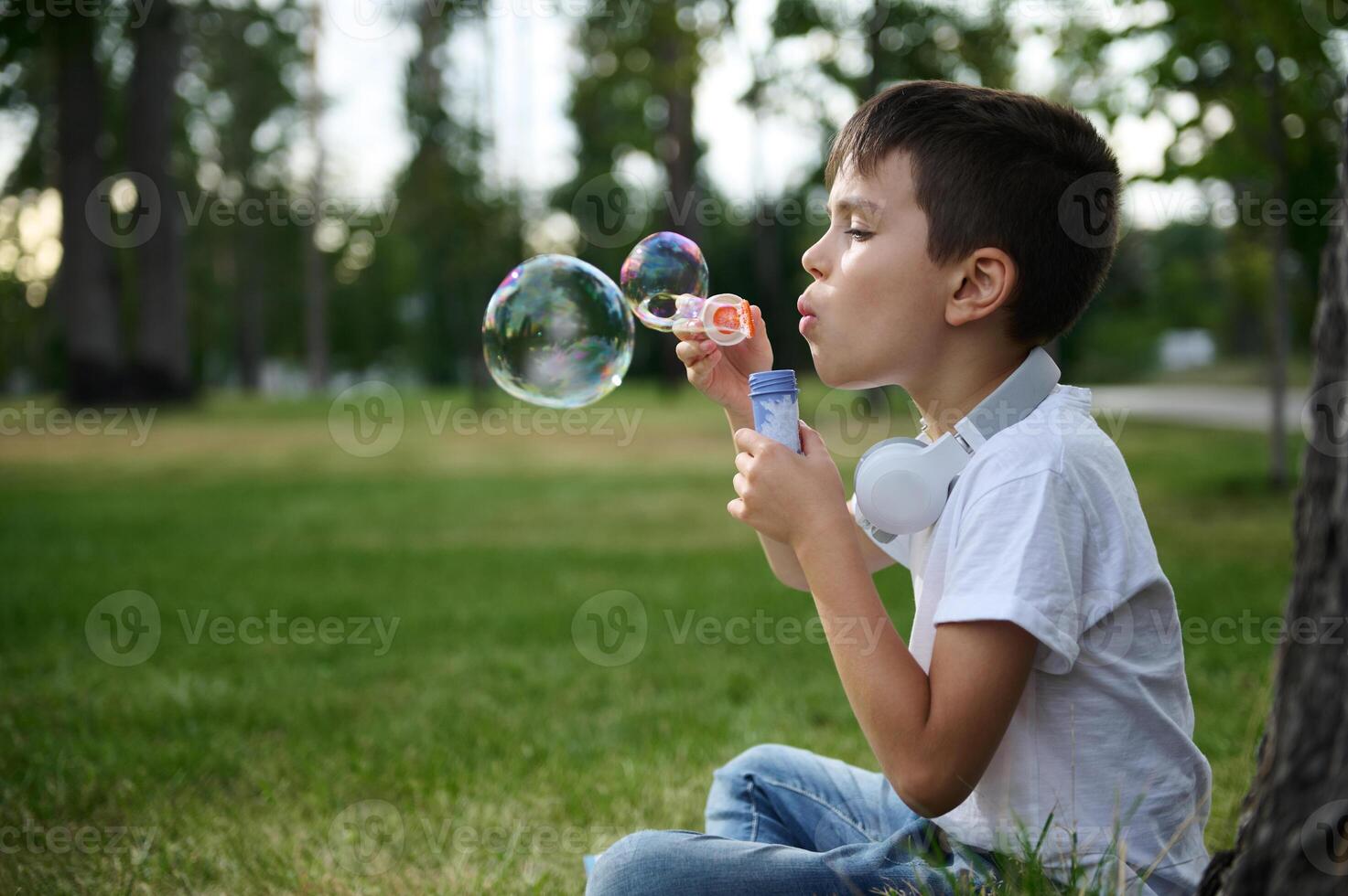 Adorable handsome preadolescent child boy blowing starting soap bubbles on the park, resting during his school recreation photo