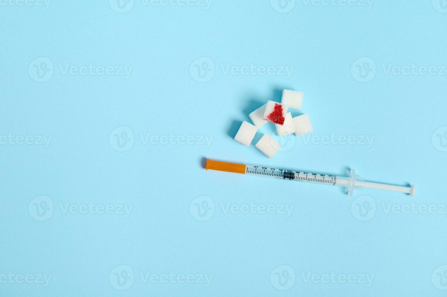 Flat lay of insulin syringe and pure refined white sugar cubes with blood drop isolated over colored blue background with copy space for medical ad. World diabetes day awareness concept, 14 November photo