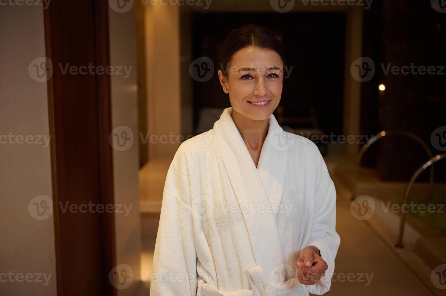 Portrait of a relaxed smiling beautiful elegant middle aged 30- 40 years old European woman in white terry robe enjoying vacation relaxing at spa resort. Recreation, body care and leisure concept photo