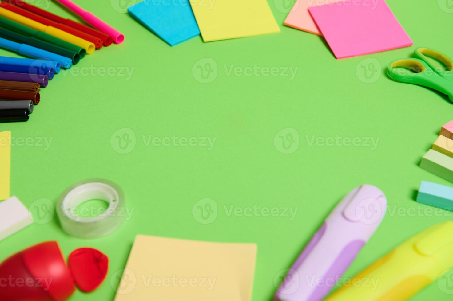 Multi colored assortment of stationery office supplies and school accessories arranged in a circle on light green background, copy space photo