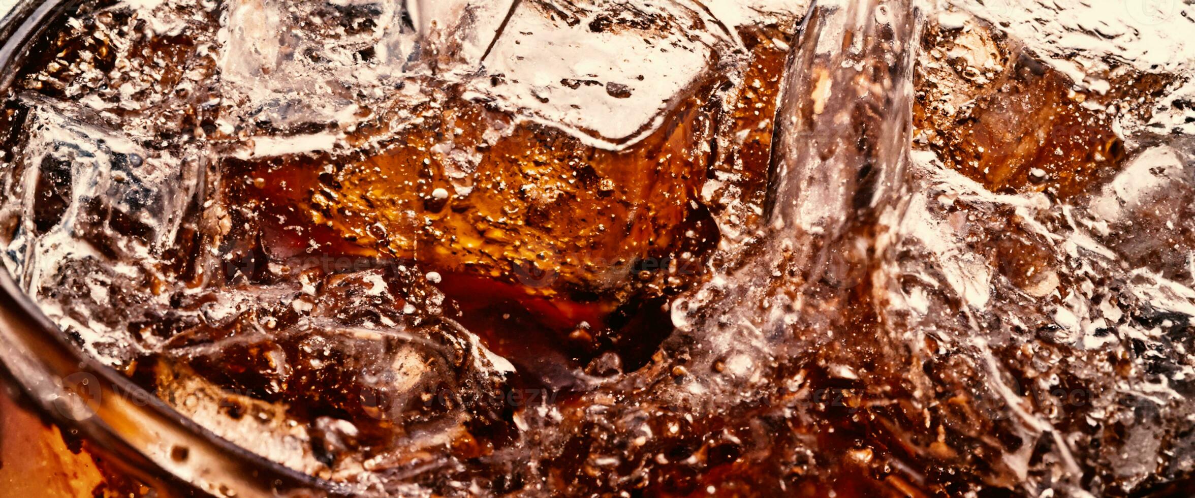 Splashing of Cola and Ice. Cola soda and ice splashing fizzing or floating up to top of surface. Close up of ice in cola water. Texture of carbonate drink with bubbles in glass. Cold drink background photo