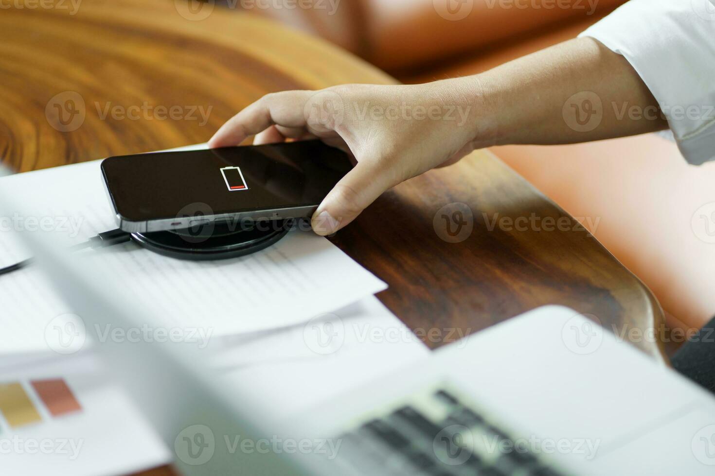 Charging mobile phone battery with wireless charging device in the table. Smartphone charging on a charging pad. Mobile phone near wireless charger Modern lifestyle technology concept photo