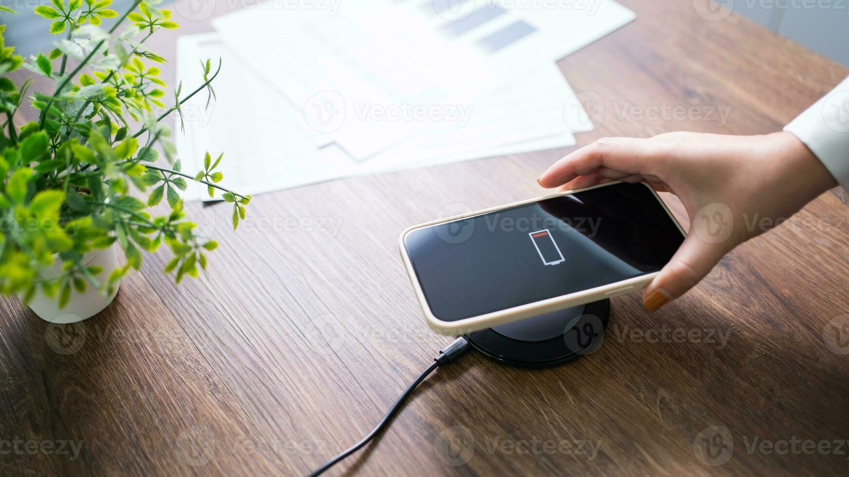 Charging mobile phone battery with wireless charging device in the table. Smartphone charging on a charging pad. Mobile phone near wireless charger Modern lifestyle technology concept. photo