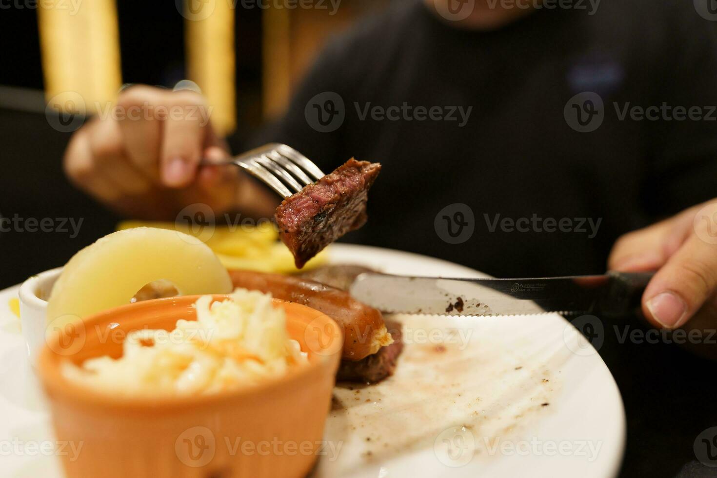 hombre comiendo A la parrilla carnes estaca desde lámina. mano participación cuchillo y tenedor corte A la parrilla carne de vaca filete foto