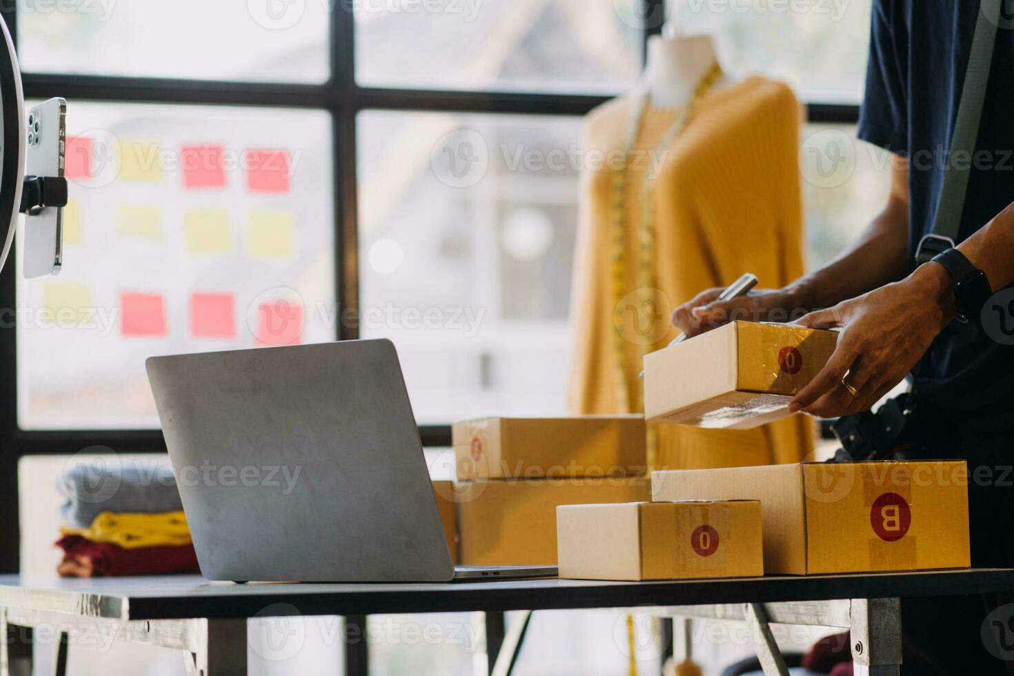 Female fashion, designer, Looking at Drawings and Sketches that are Pinned to the Wall Behind Her Desk. Studio is Sunny. Personal Computer, Colorful Fabrics, Sewing Items are Visible. photo