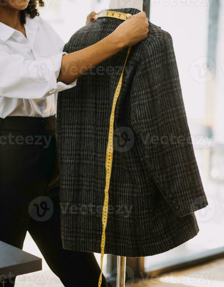 Female fashion, designer, Looking at Drawings and Sketches that are Pinned to the Wall Behind Her Desk. Studio is Sunny. Personal Computer, Colorful Fabrics, Sewing Items are Visible. photo