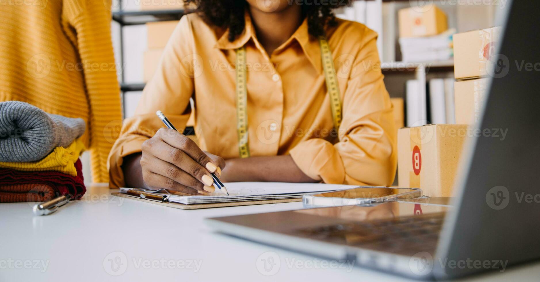 Female fashion, designer, Looking at Drawings and Sketches that are Pinned to the Wall Behind Her Desk. Studio is Sunny. Personal Computer, Colorful Fabrics, Sewing Items are Visible. photo