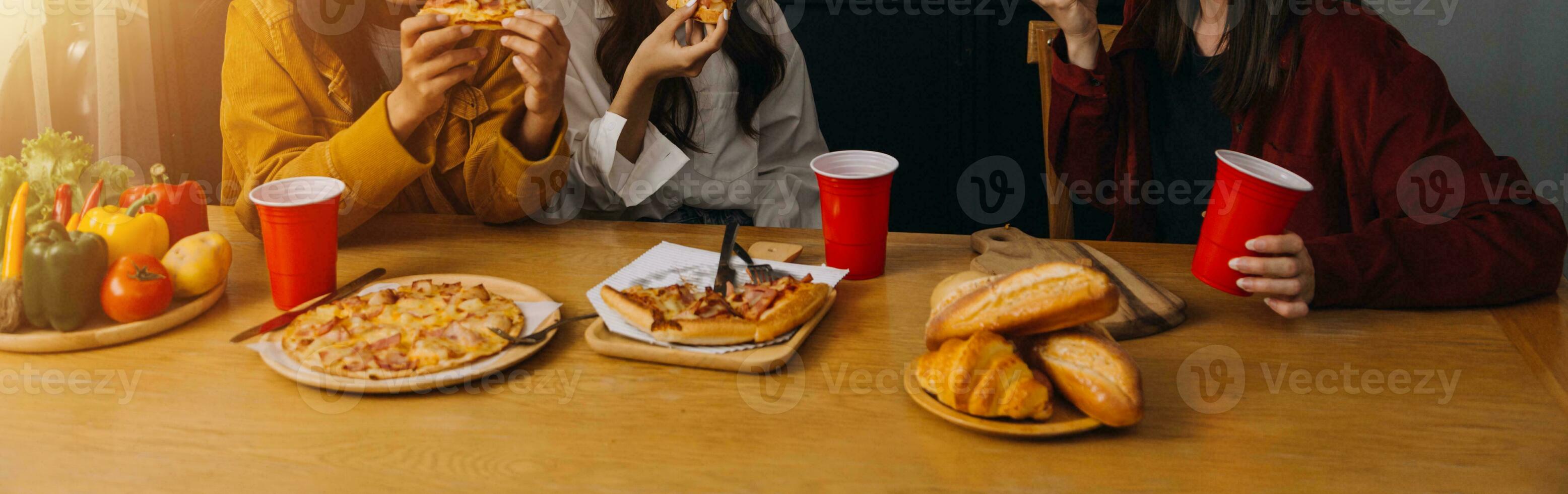 Laughing group of diverse young woman hanging out at home together and eating pizza photo
