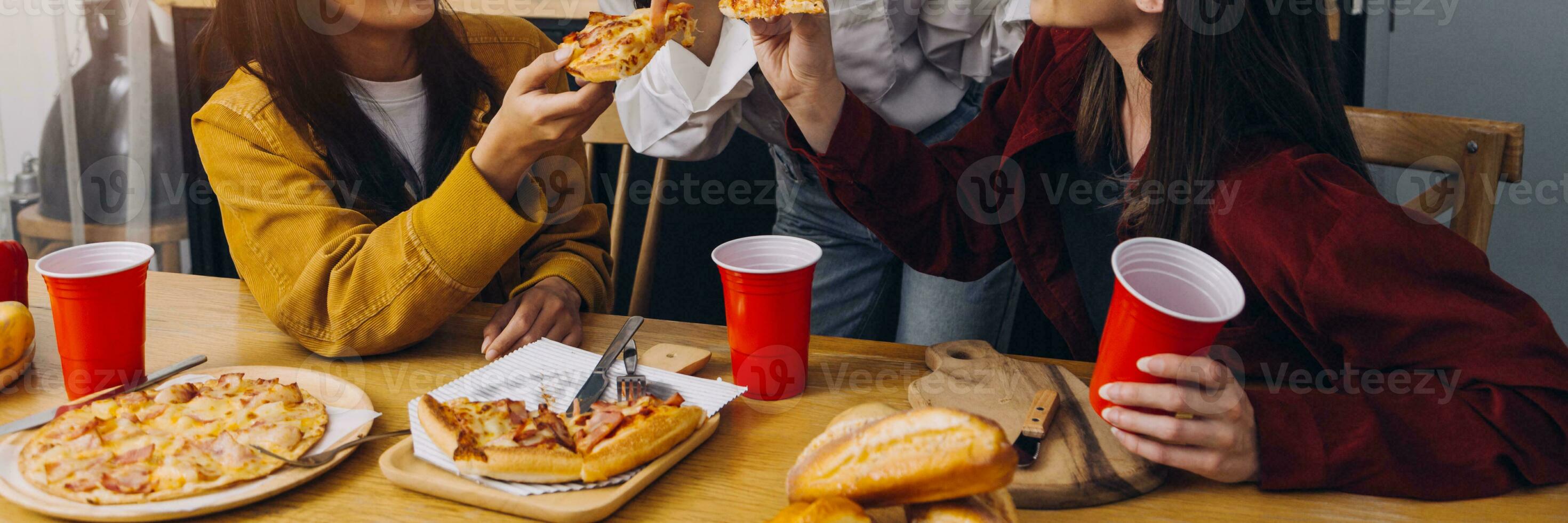 Laughing group of diverse young woman hanging out at home together and eating pizza photo