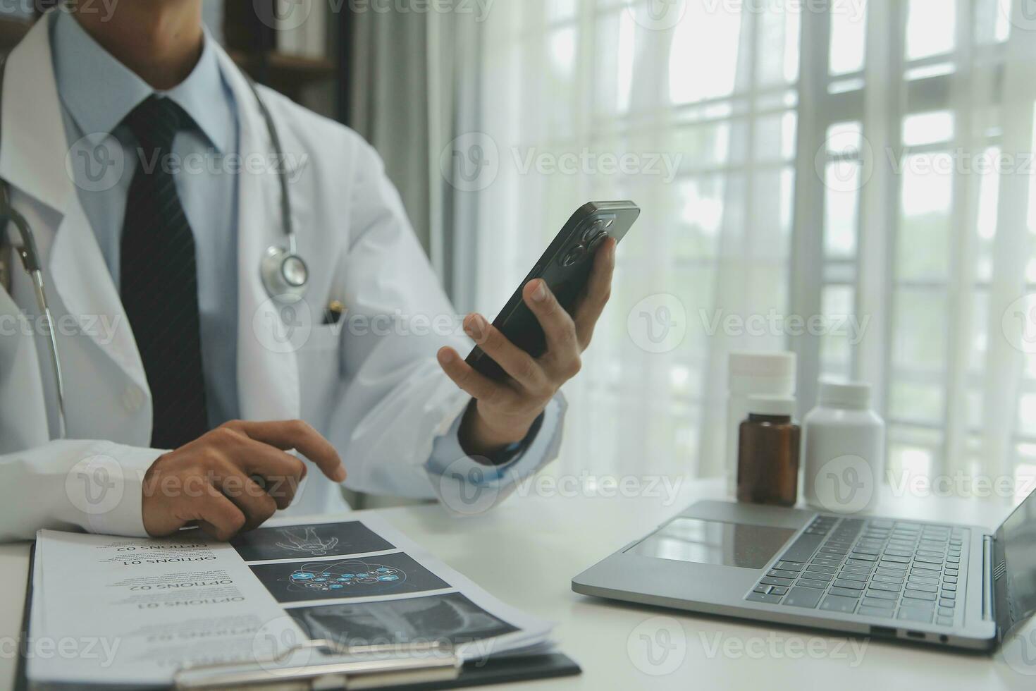 Confident doctor man holding a pill bottle and writing while talking with senior patient and reviewing his medication at office room. photo