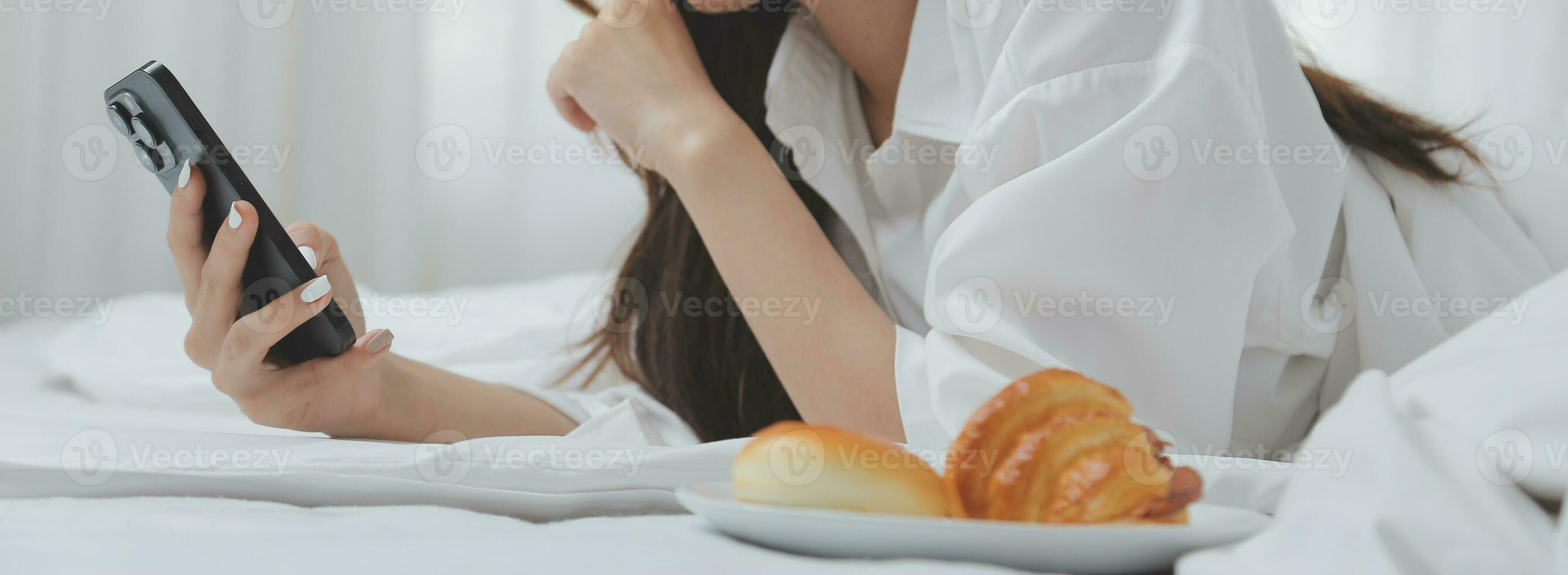 Happy young female in casual clothes smiling and looking at camera while using laptop on bed in bedroom at home photo