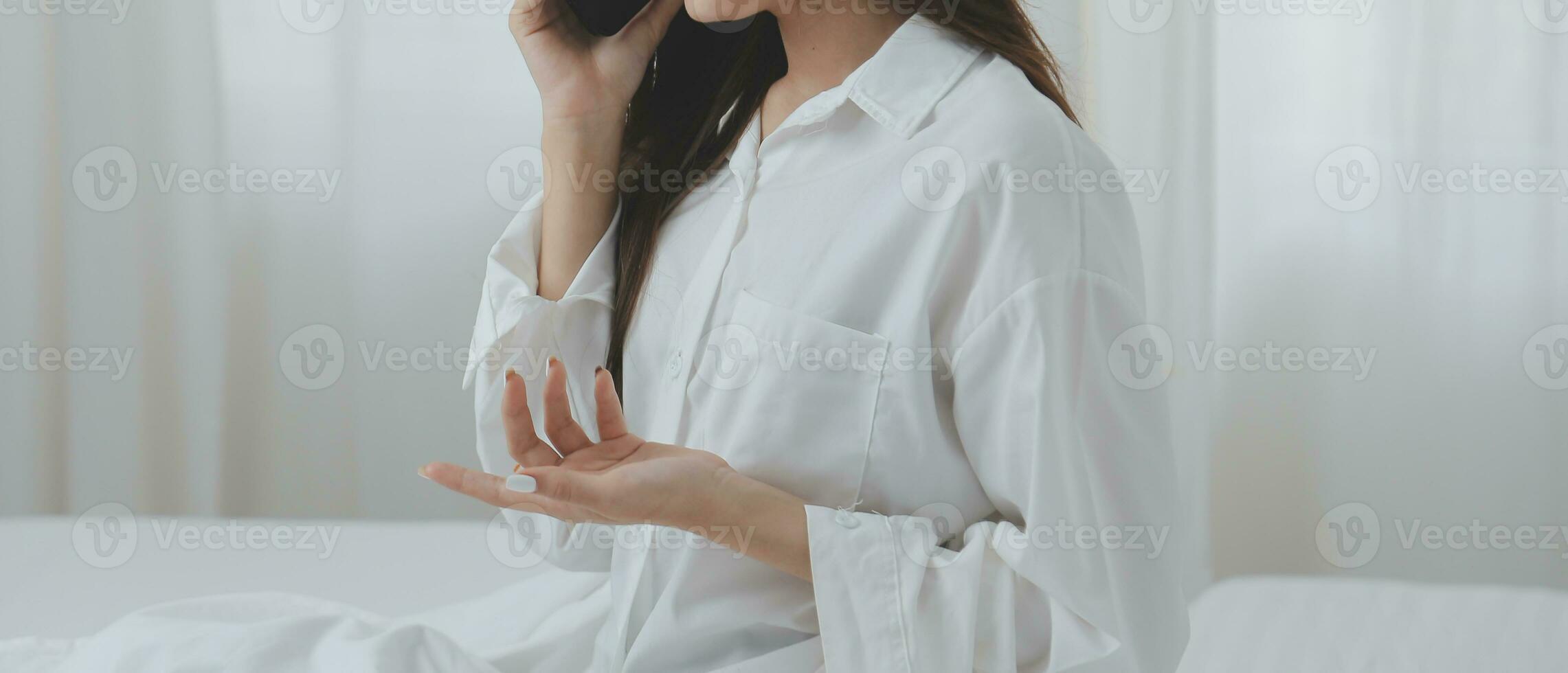 Happy young female in casual clothes smiling and looking at camera while using laptop on bed in bedroom at home photo