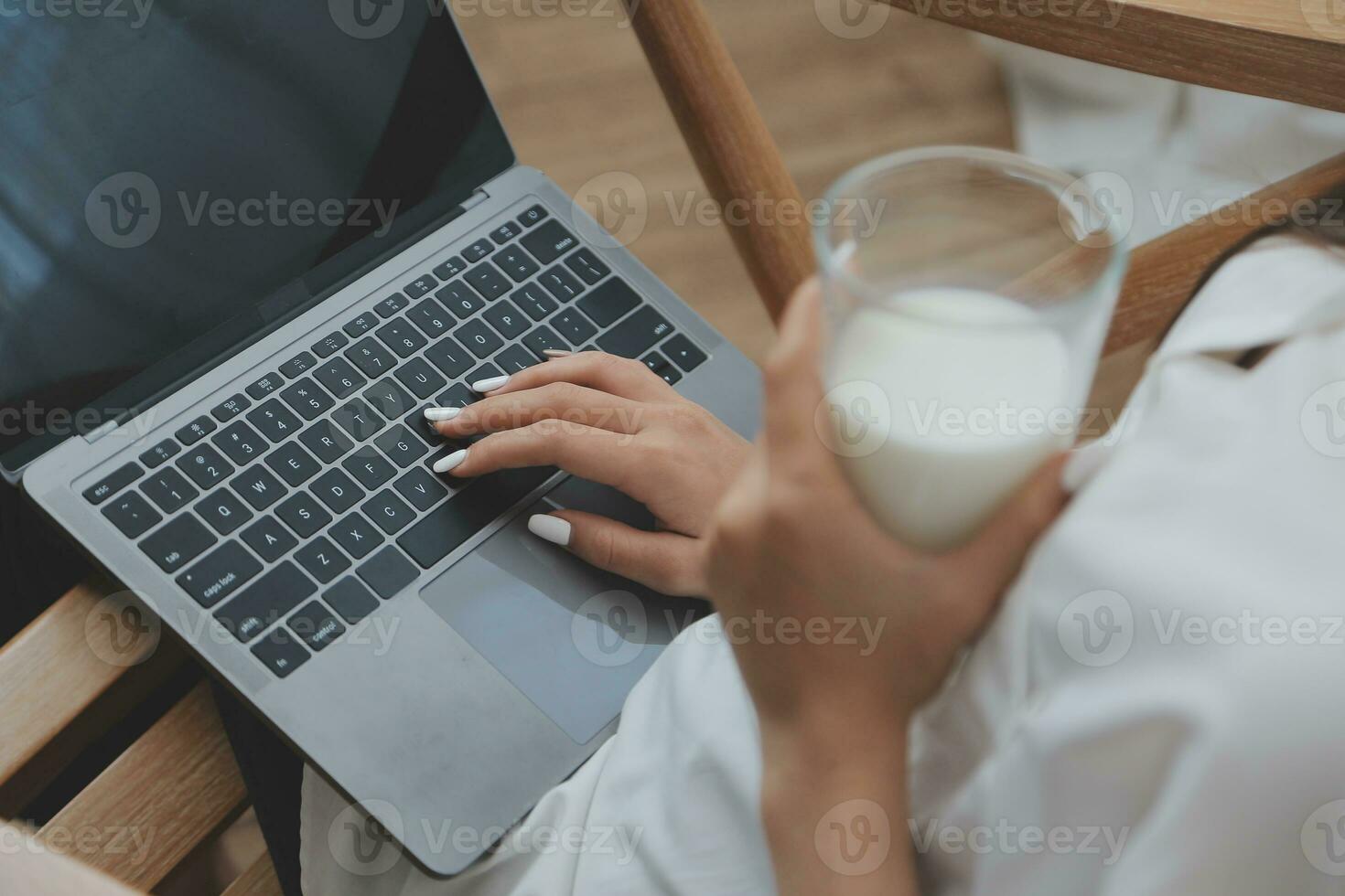 Happy young female in casual clothes smiling and looking at camera while using laptop on bed in bedroom at home photo