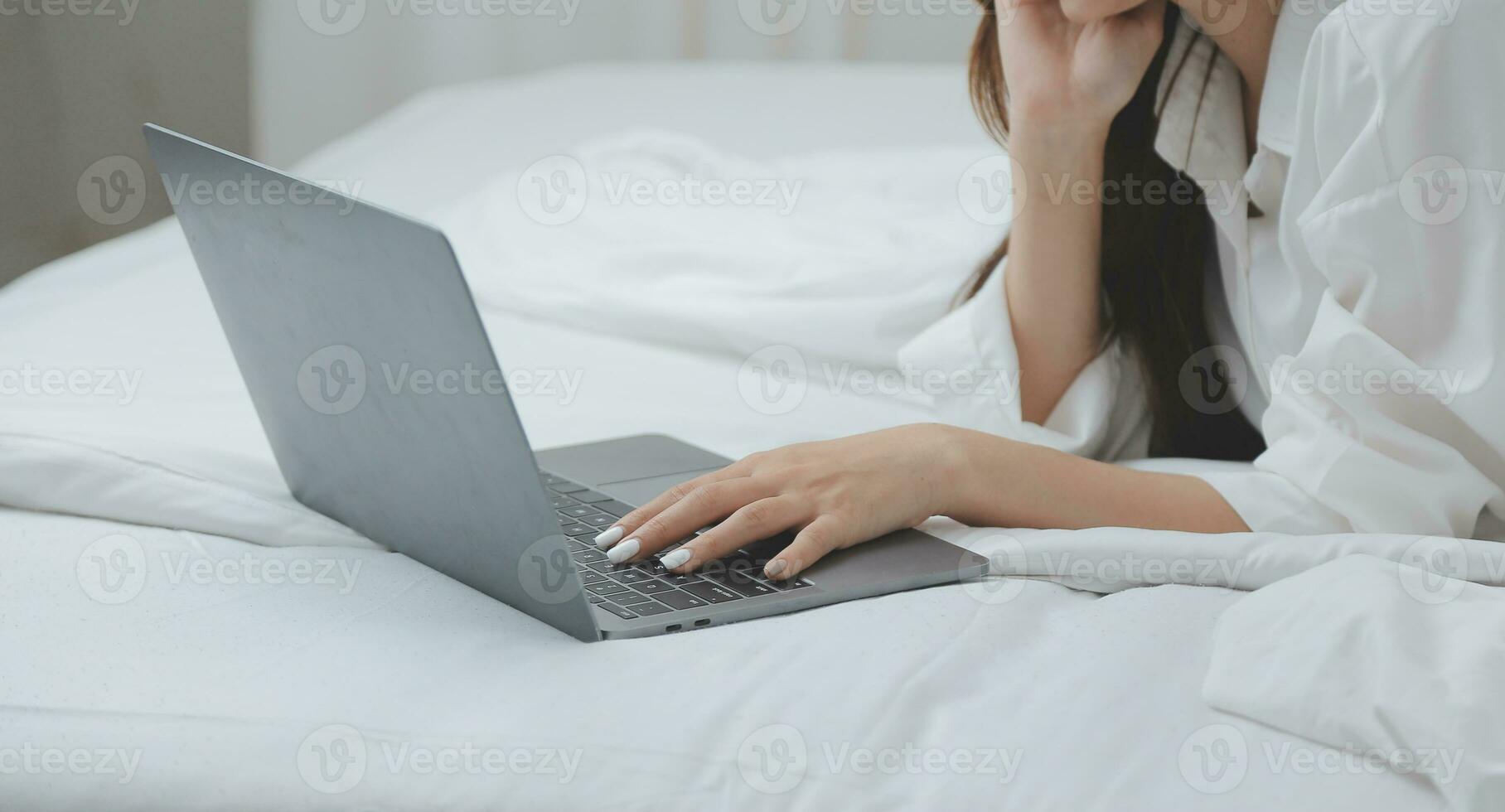 Happy young female in casual clothes smiling and looking at camera while using laptop on bed in bedroom at home photo
