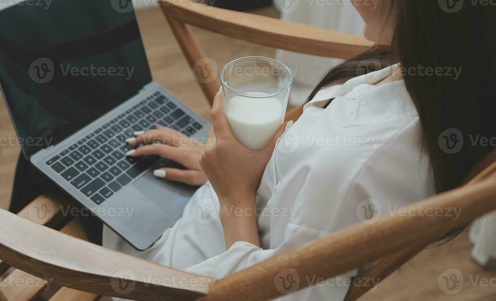 Happy young female in casual clothes smiling and looking at camera while using laptop on bed in bedroom at home photo