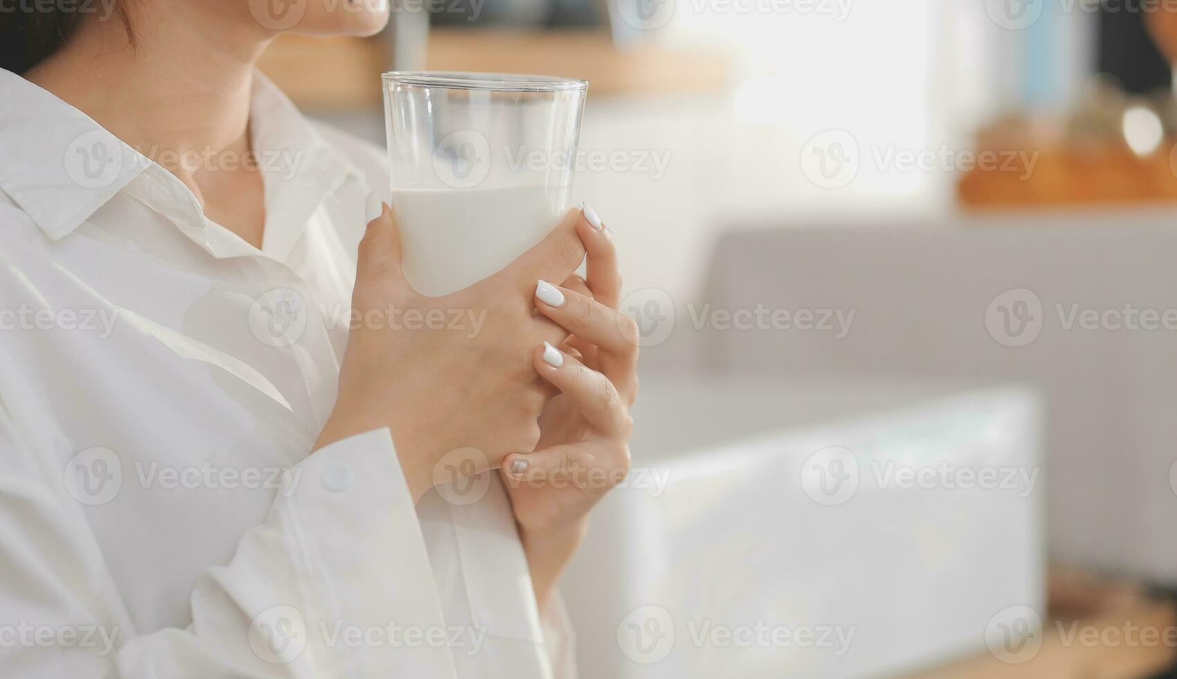 Portrait of a satisfied young asian woman drinking milk from the glass isolated over white background photo