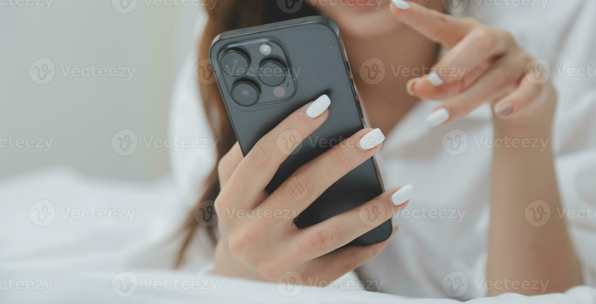 Happy young female in casual clothes smiling and looking at camera while using laptop on bed in bedroom at home photo