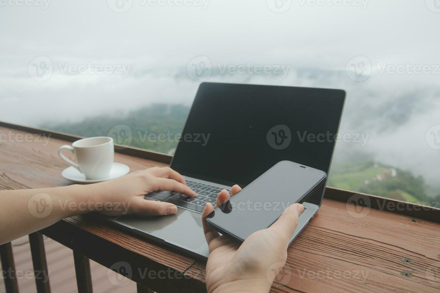 Young man freelancer traveler wearing hat anywhere working online using laptop and enjoying mountains view photo