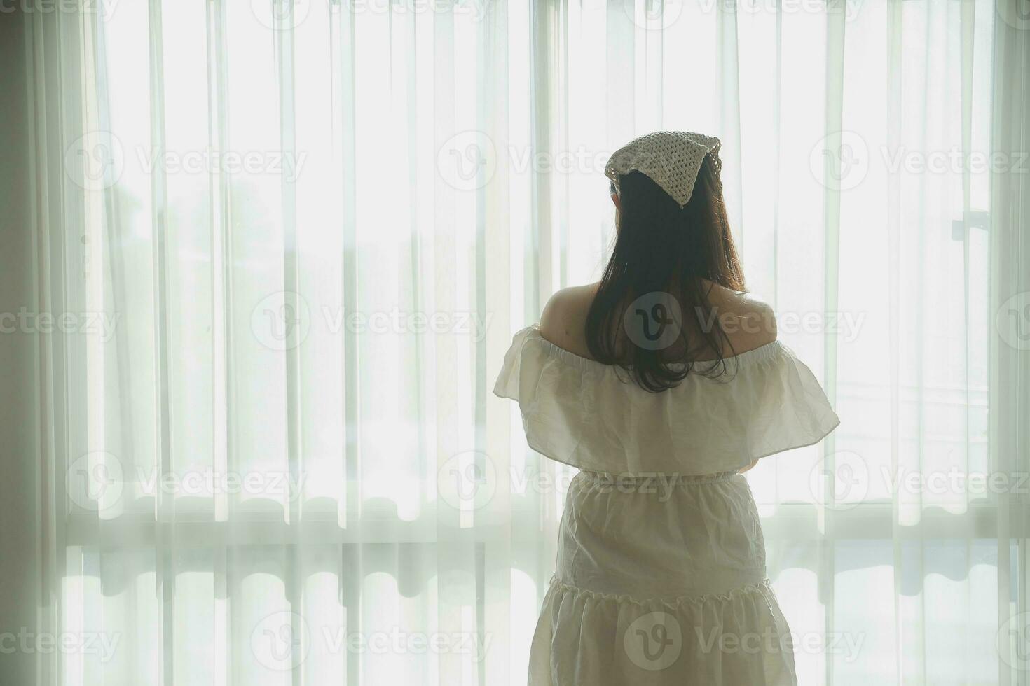 silhouette of woman sitting on the bed beside the windows with sunlight in the morning photo