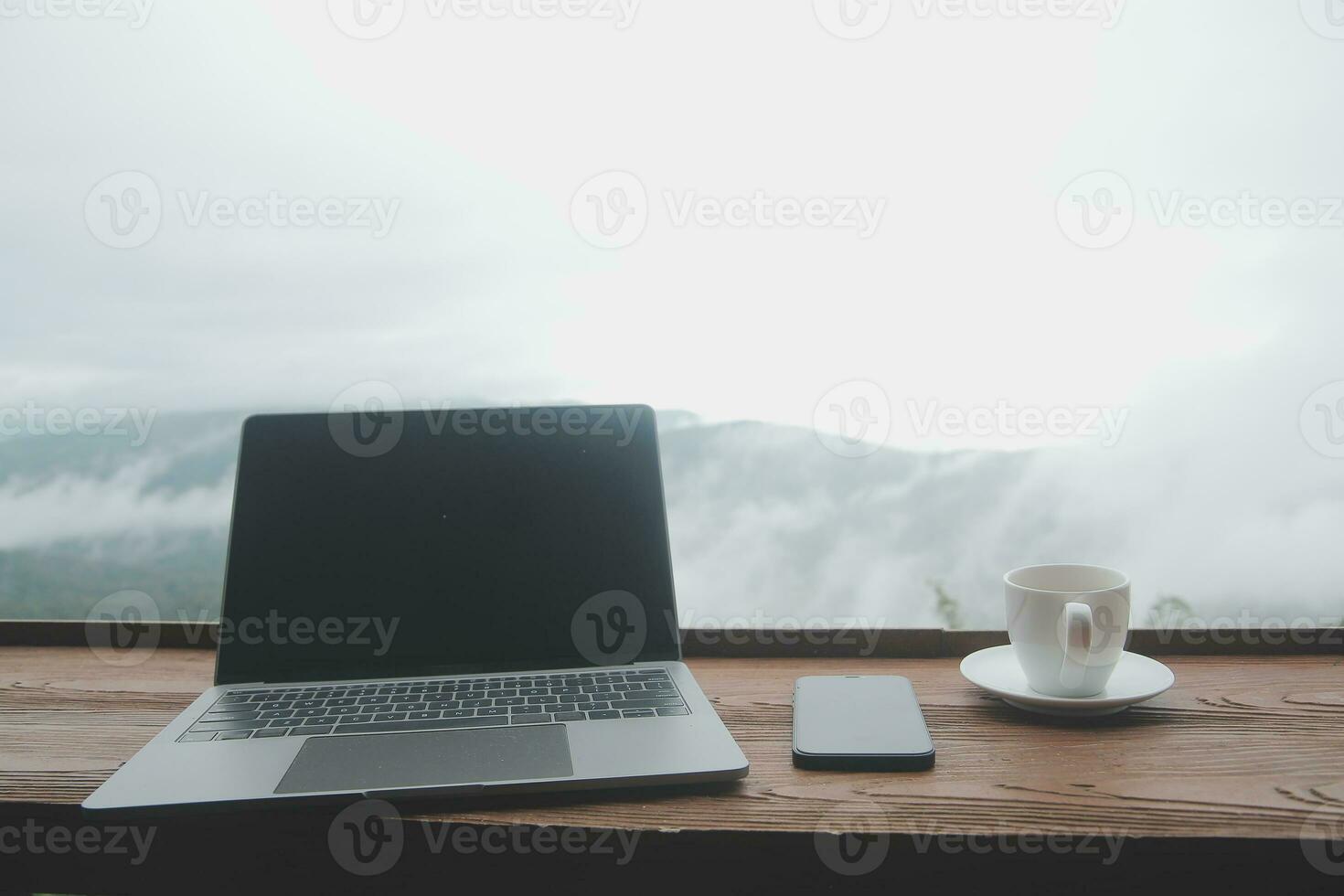 Young man freelancer traveler wearing hat anywhere working online using laptop and enjoying mountains view photo