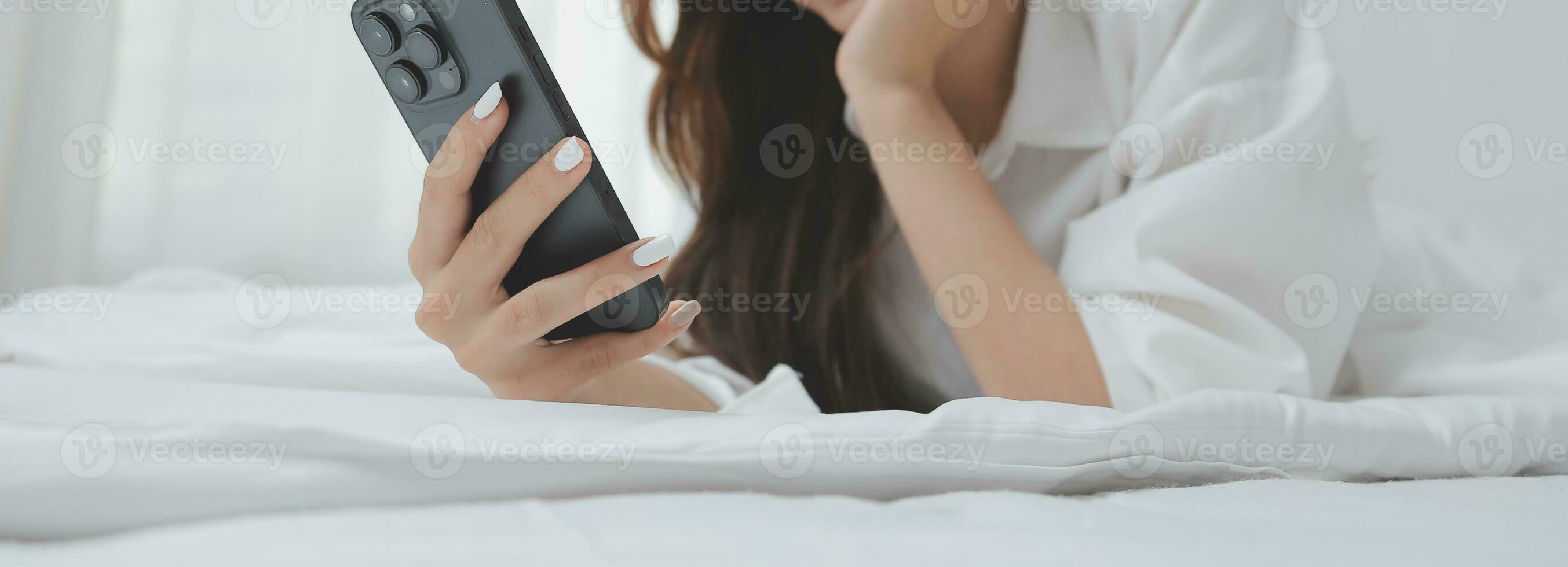 Happy young female in casual clothes smiling and looking at camera while using laptop on bed in bedroom at home photo