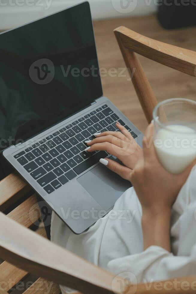 Happy young female in casual clothes smiling and looking at camera while using laptop on bed in bedroom at home photo