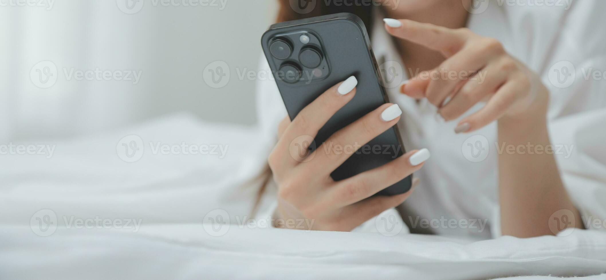 Happy young female in casual clothes smiling and looking at camera while using laptop on bed in bedroom at home photo