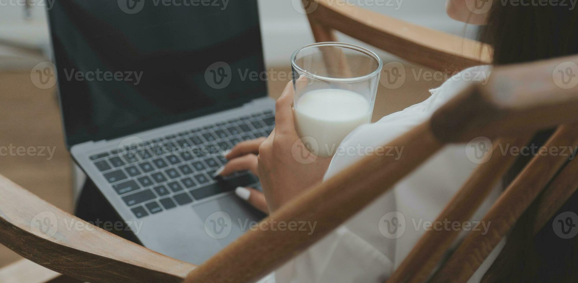 Happy young female in casual clothes smiling and looking at camera while using laptop on bed in bedroom at home photo