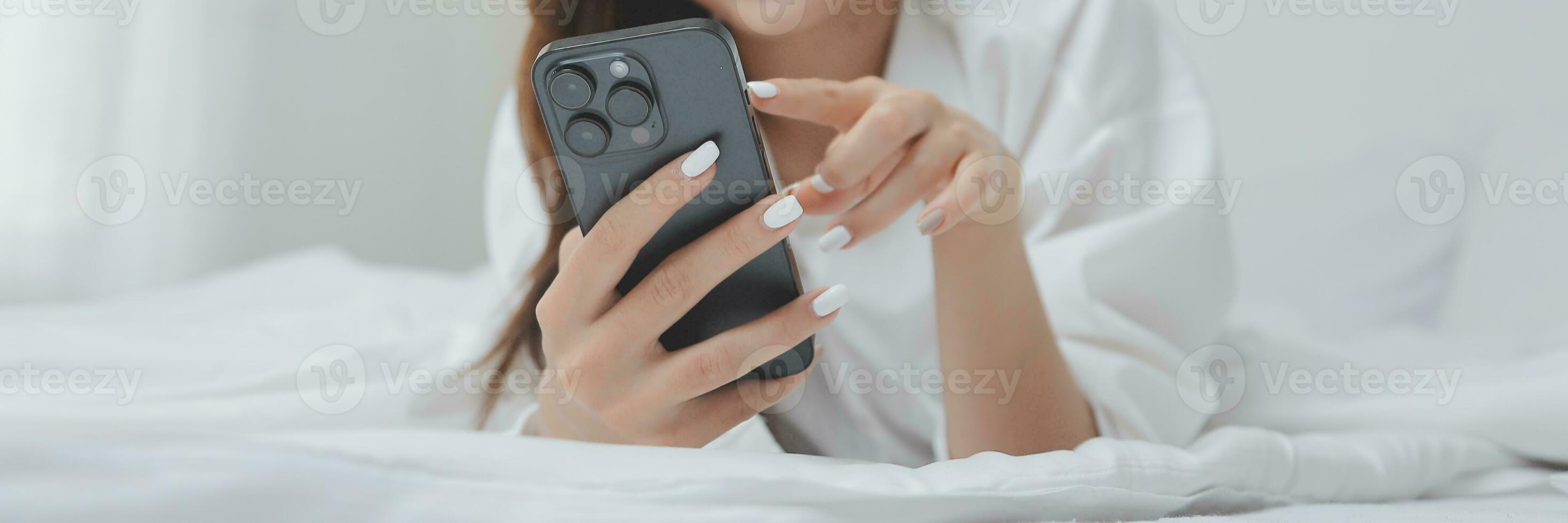 Happy young female in casual clothes smiling and looking at camera while using laptop on bed in bedroom at home photo