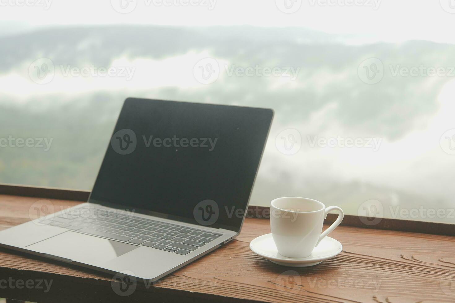 Young man freelancer traveler wearing hat anywhere working online using laptop and enjoying mountains view photo