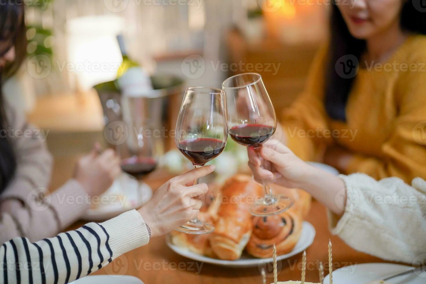 Cheerful friends enjoying home Birthday holiday party. Asian sister cheering drinking red wine celebrating with Birthday cake. photo