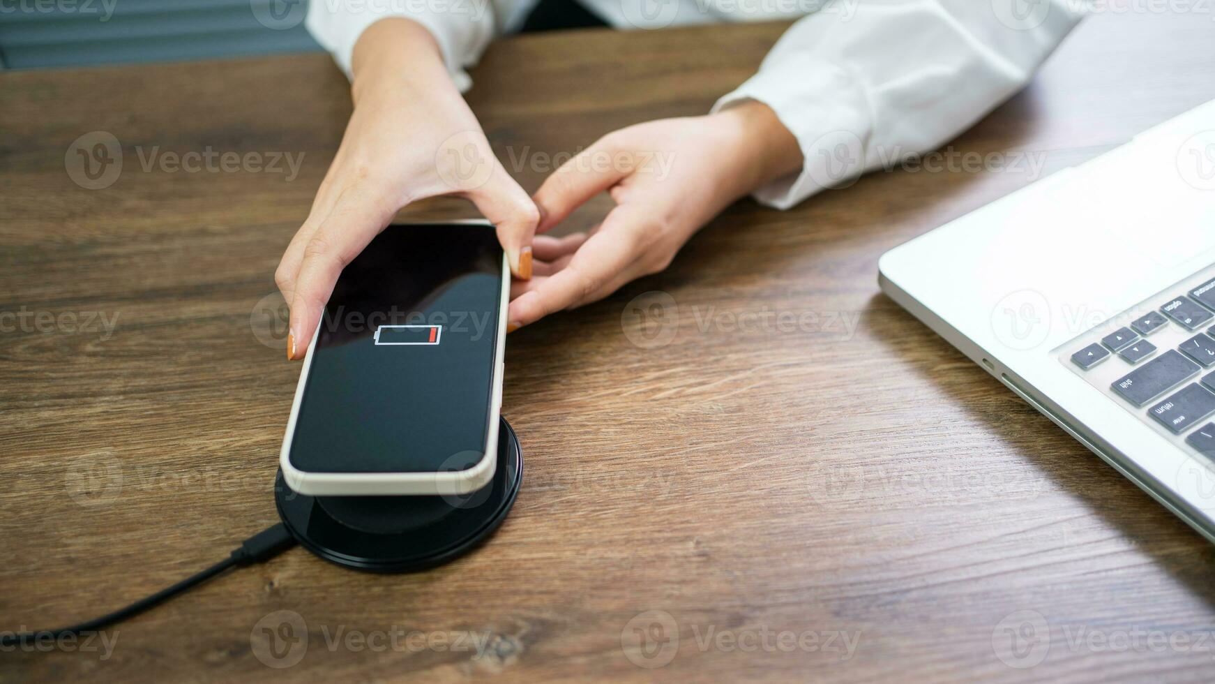 Charging mobile phone battery with wireless charging device in the table. Smartphone charging on a charging pad. Mobile phone near wireless charger Modern lifestyle technology concept. photo
