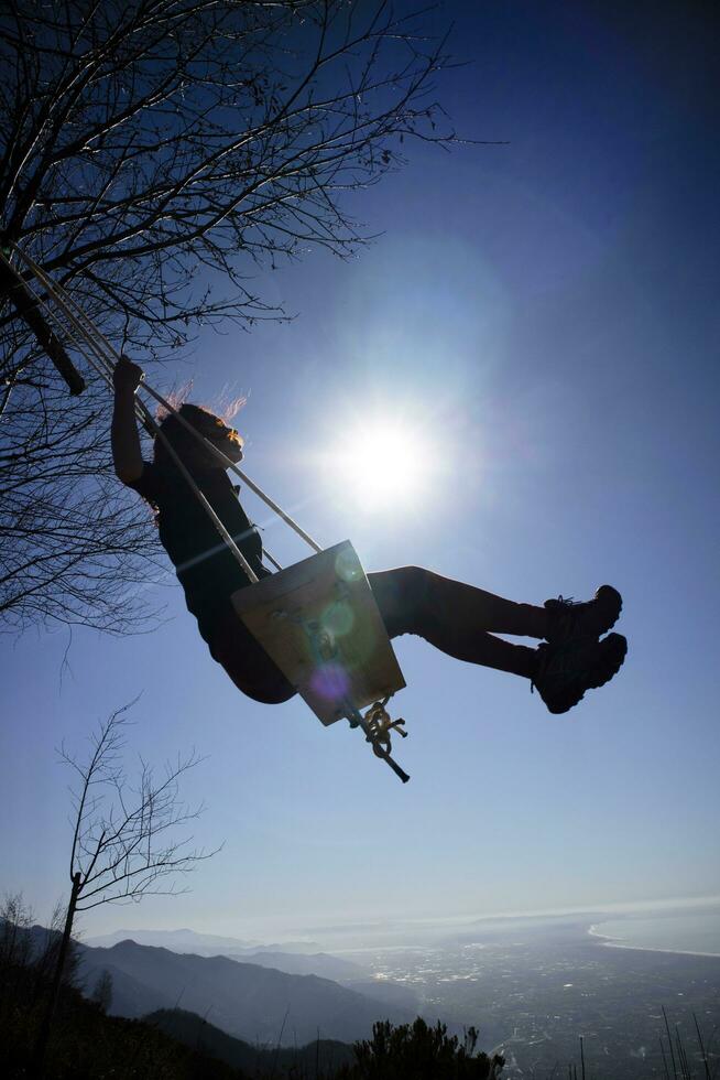 Girl shot against the light while having fun on the swing photo