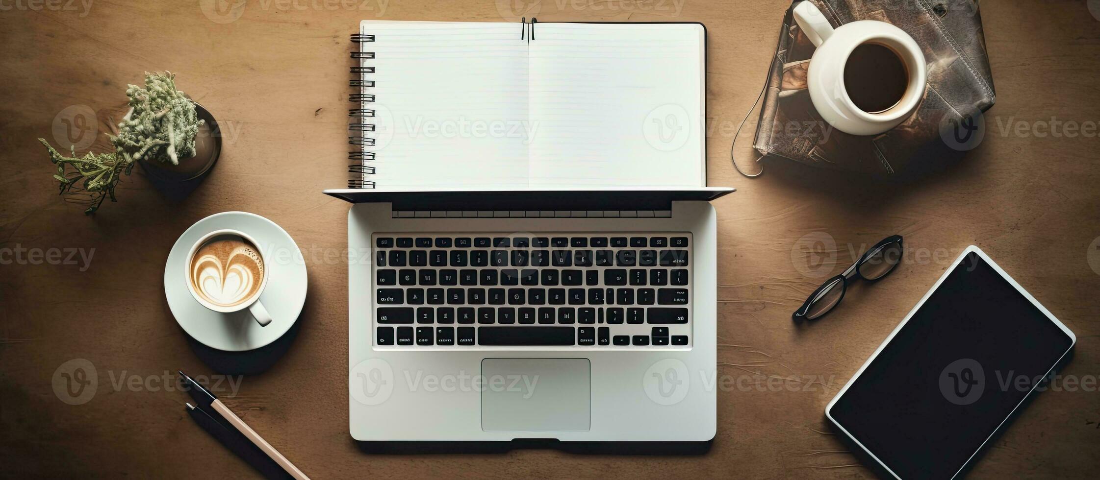 A photograph taken from above showing a workspace desk with a laptop, notebook, coffee mug, photo