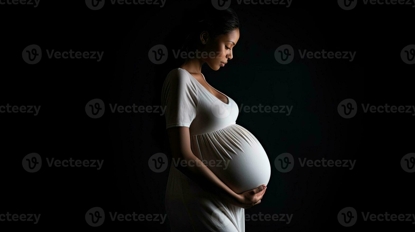 Pregnant woman in white dress close up of belly Studio pregnancy shoot black background photo