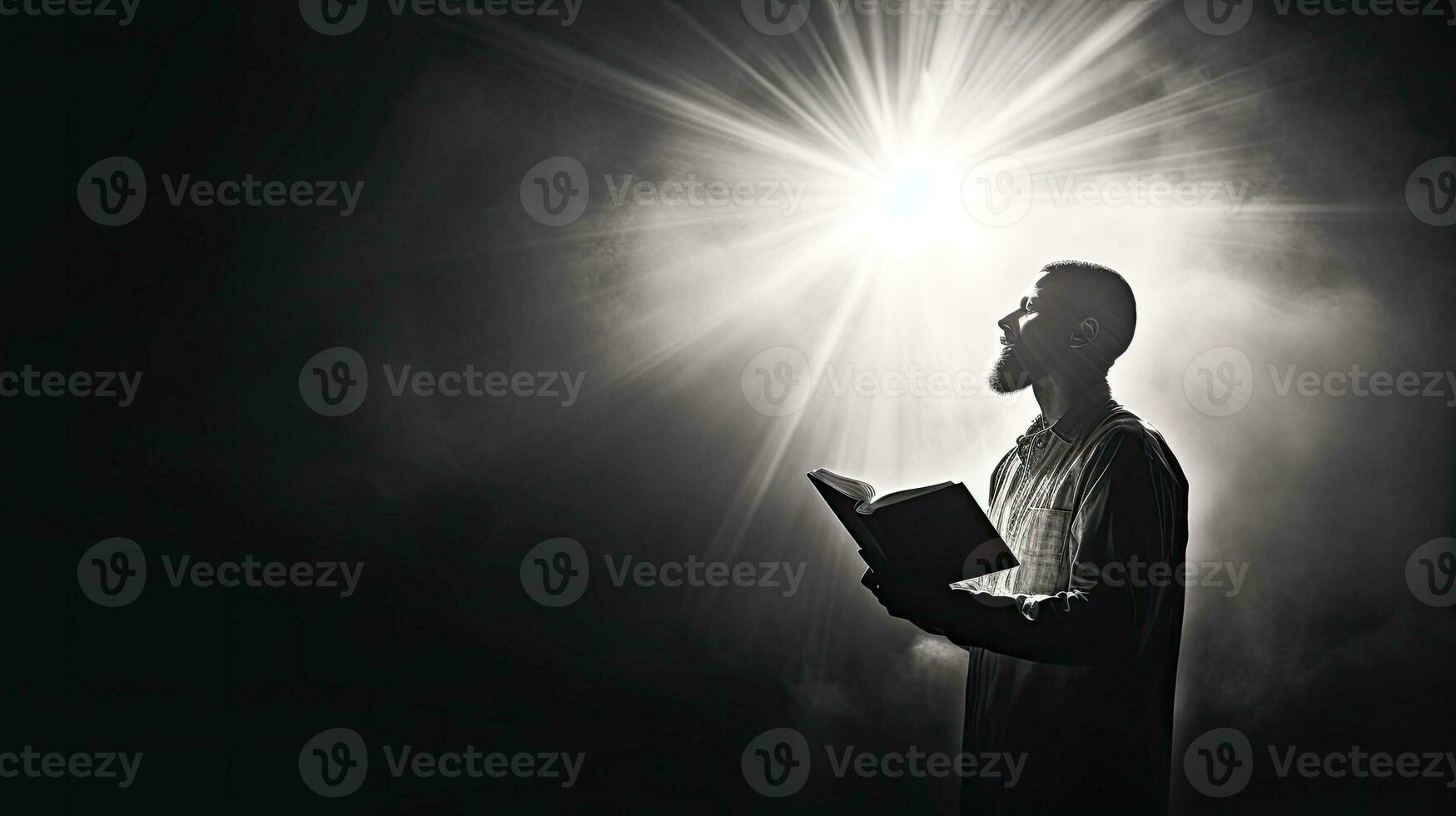 A man holds a Bible prays in black and white with a light flare photo