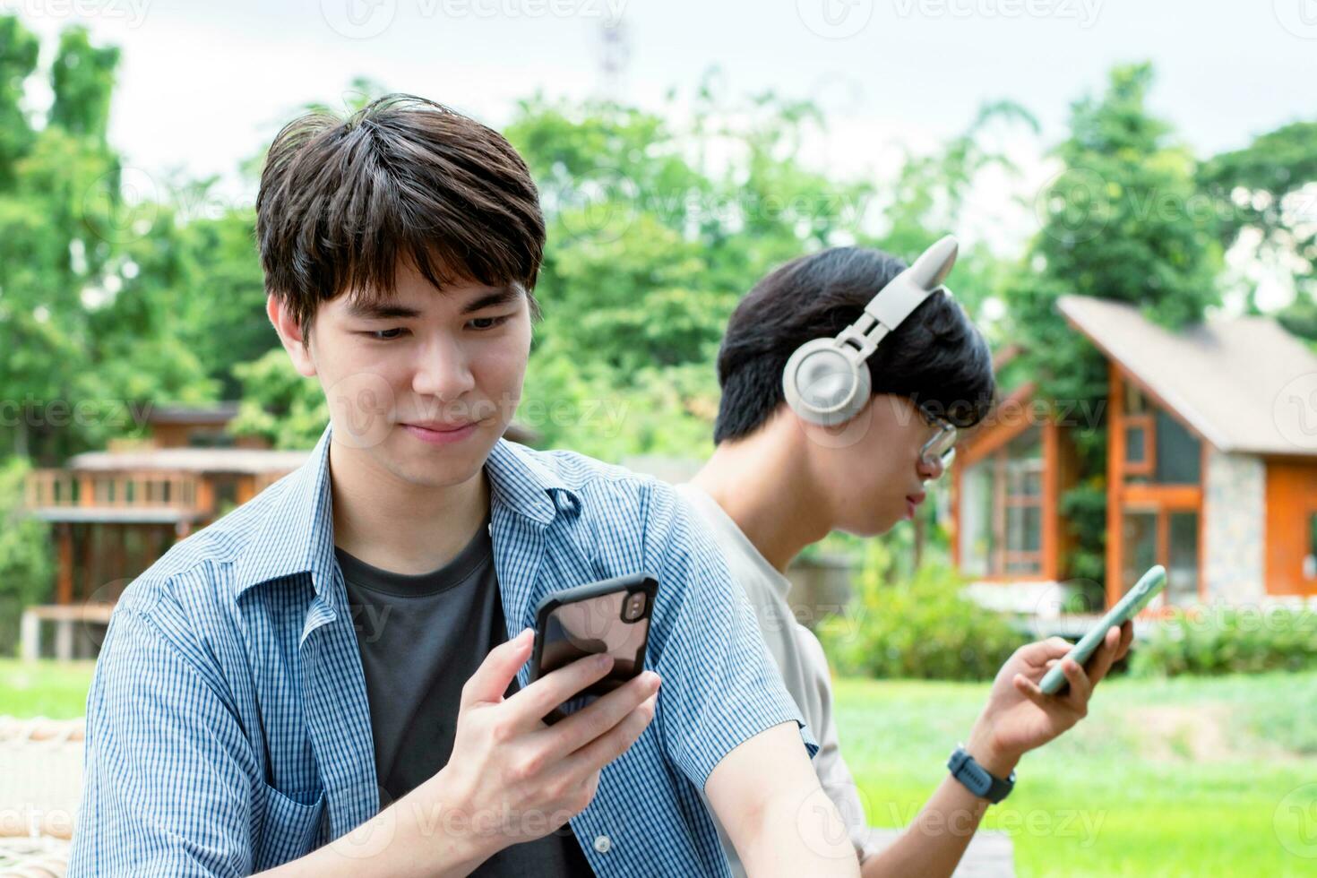 young asian adult couple wearing headphones, sitting, listening to music and spending free time together in front of their house, good relationship and best friends concept. photo