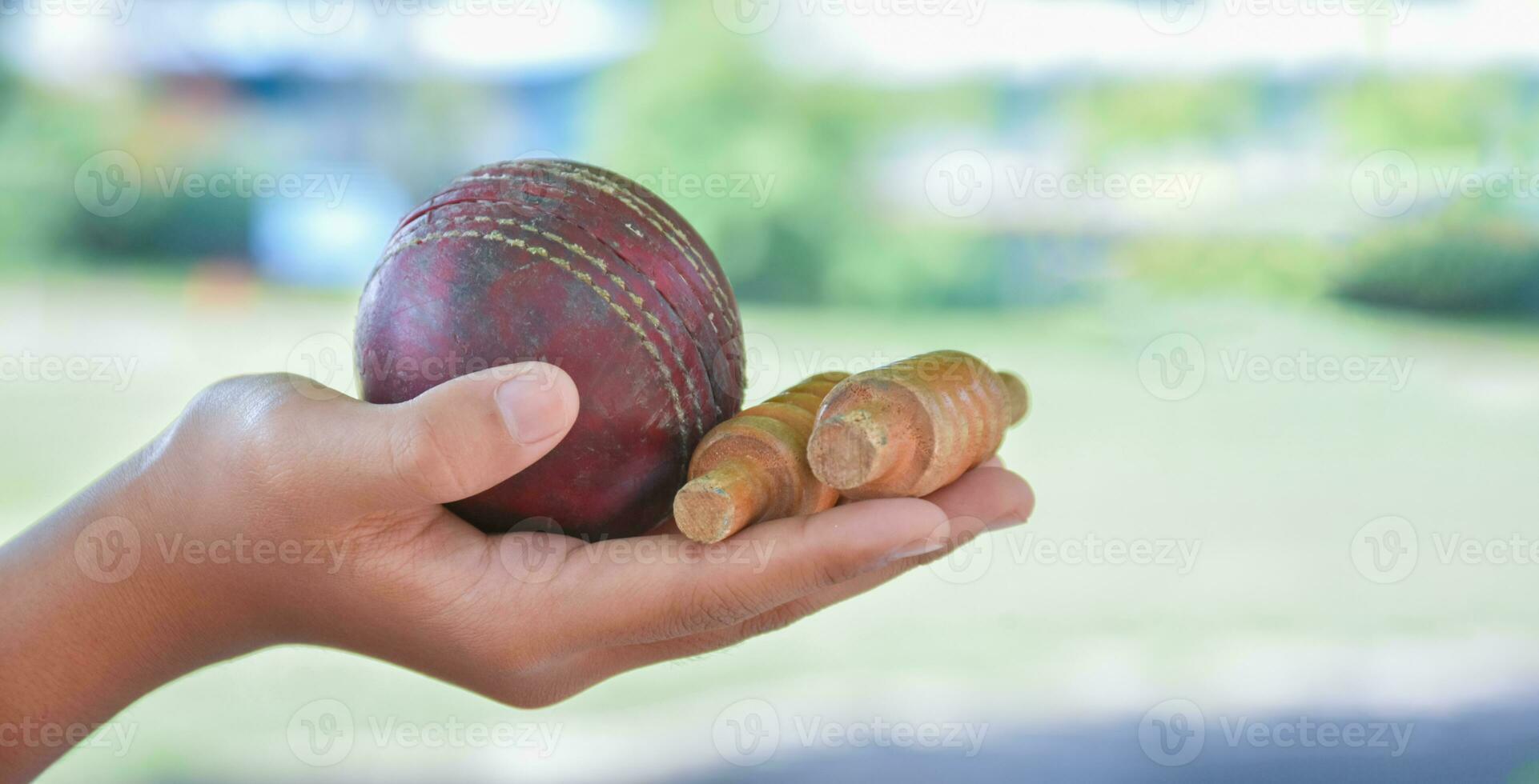 Old leather cricket ball holding in hand of student in front of school cricket court, soft and selective focus on ball, traditional sport and cricket sport lover around the world concept. photo