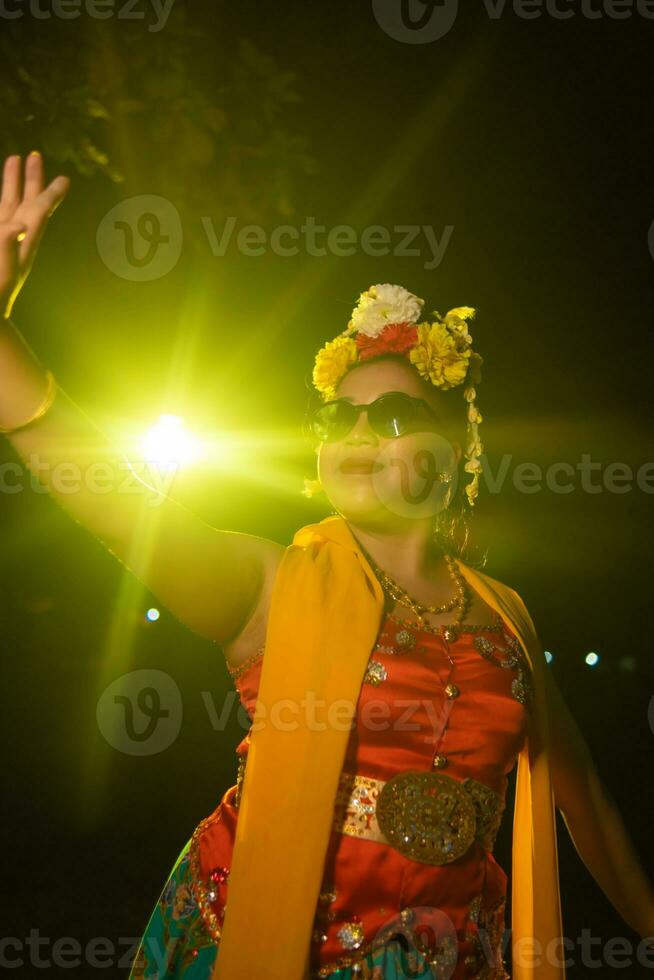 un hermosa sundanés bailarín poses y bailes en un atractivo vestir y bufanda en frente de el etapa ligero foto