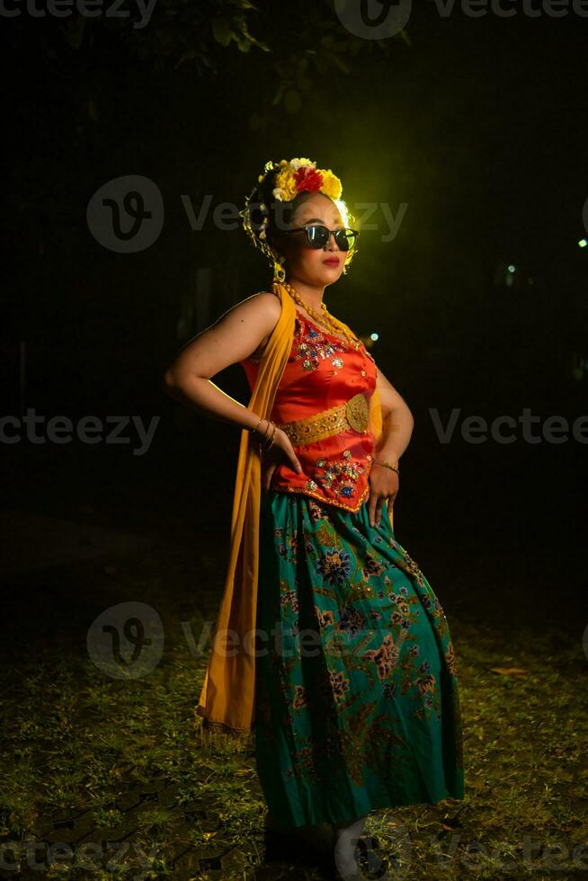 a beautiful Sundanese dancer poses and dances in a glamorous dress and scarf in front of the stage light photo