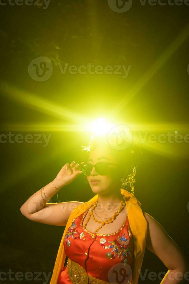 a beautiful Sundanese dancer poses and dances in a glamorous dress and scarf in front of the stage light photo