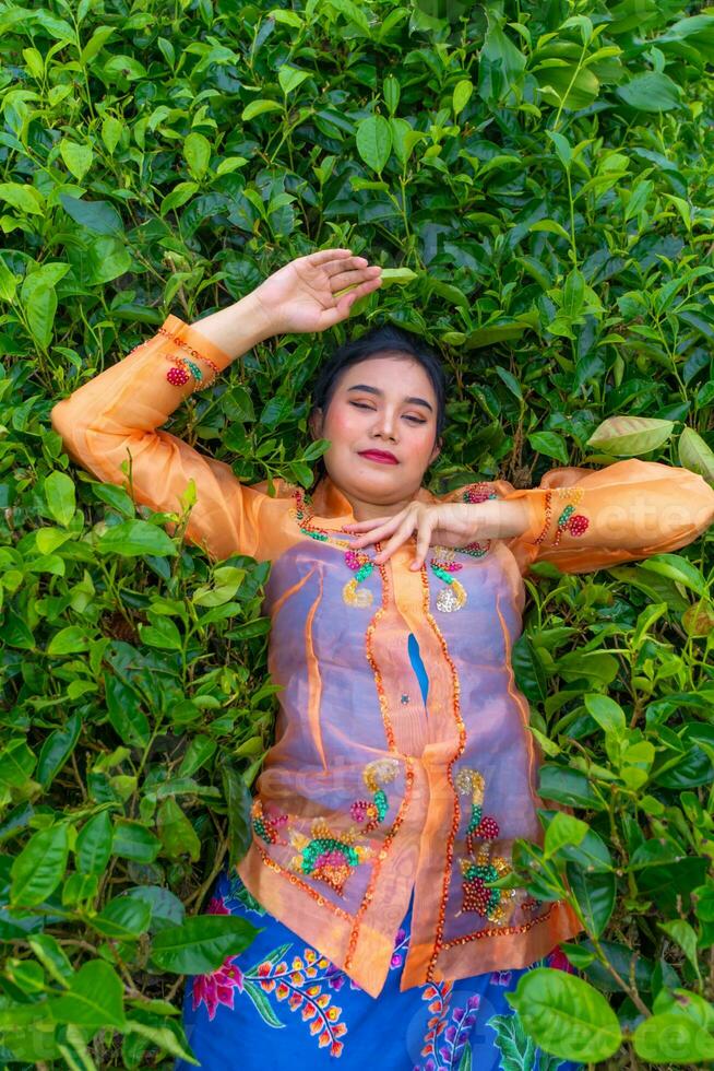 un indonesio mujer es acostado en un verde té jardín mientras en vacaciones foto