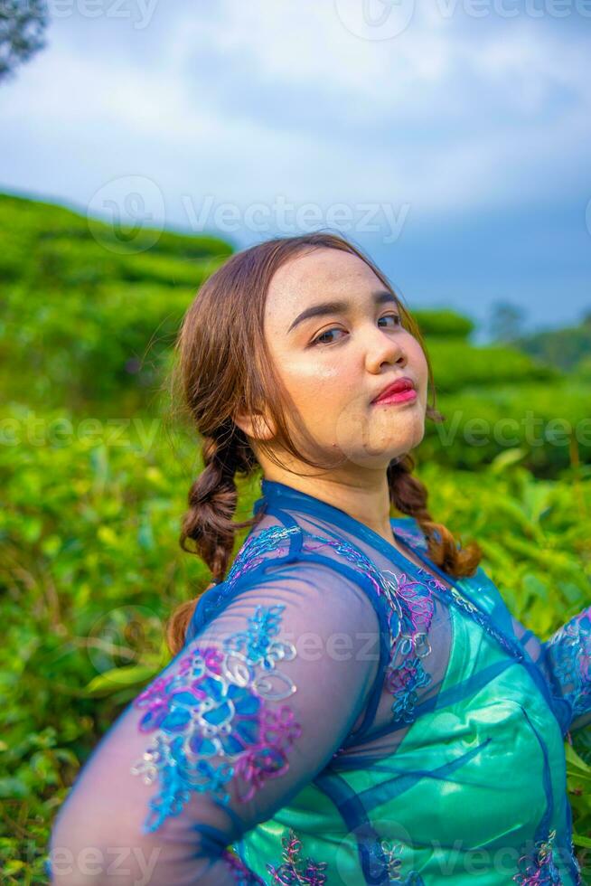 un hermosa asiático mujer es posando en su azul vestir en frente de un parque foto