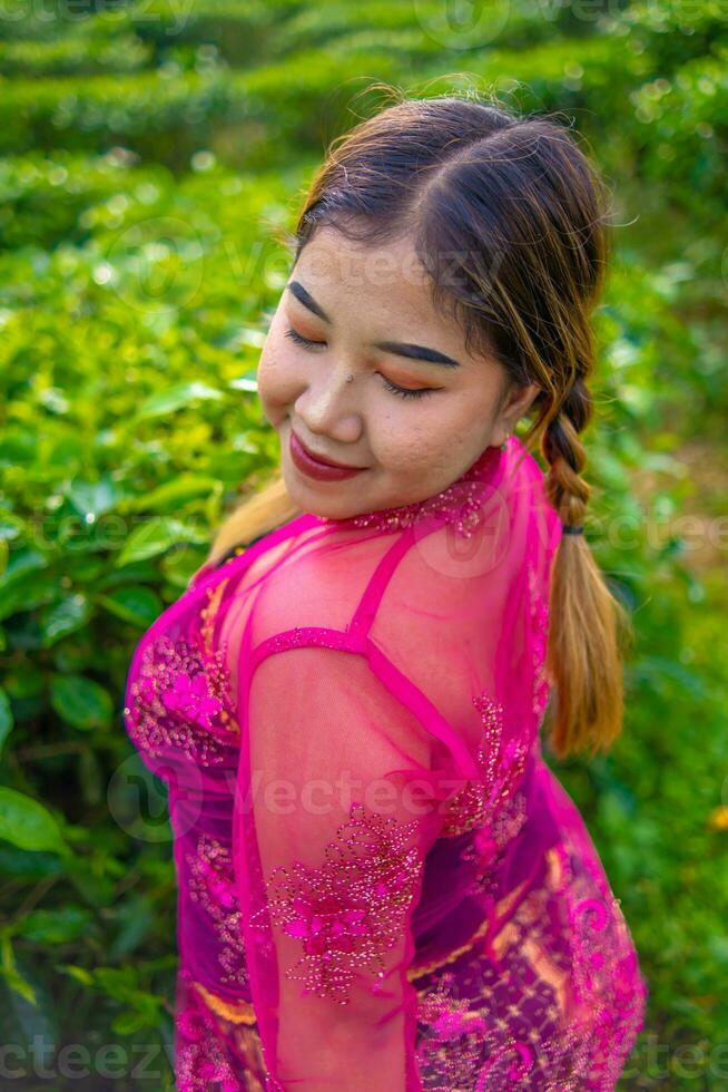 an Asian woman in a pink costume is posing in front of a tea plantation photo