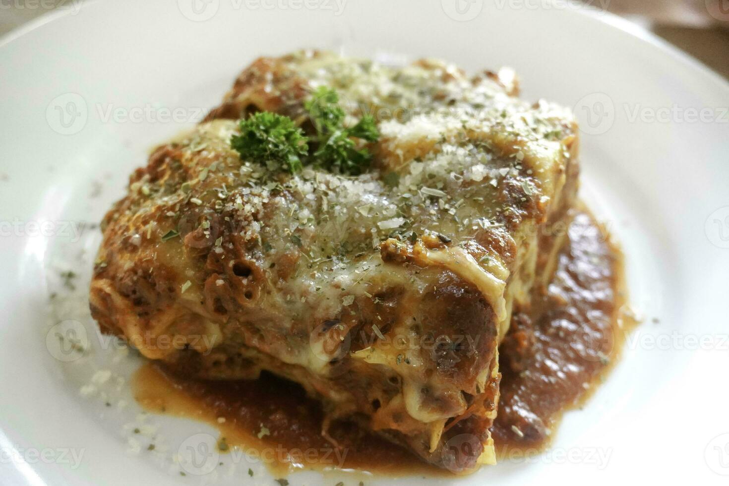 Piece of tasty hot lasagna served with a basil leaf on a white plate. Italian cuisine, menu, recipe. Homemade meat lasagna. Close up, side view photo